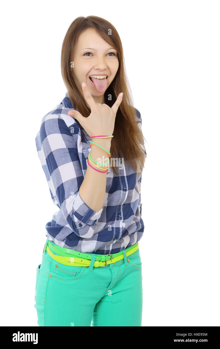 Teenage girl shows tongue and makes hand horns. Mint-colored pants and a plaid shirt. two identical belts in complimentary colours.  One person, teena Stock Photo