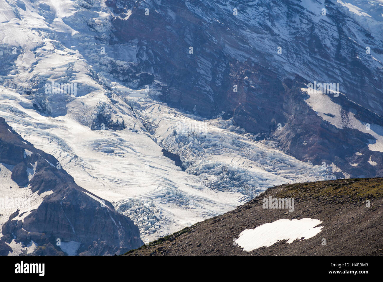 Two people standing on a ridge provide a scale illustrating massive glaciers and icefalls on Mount Rainier's north-east face. Stock Photo