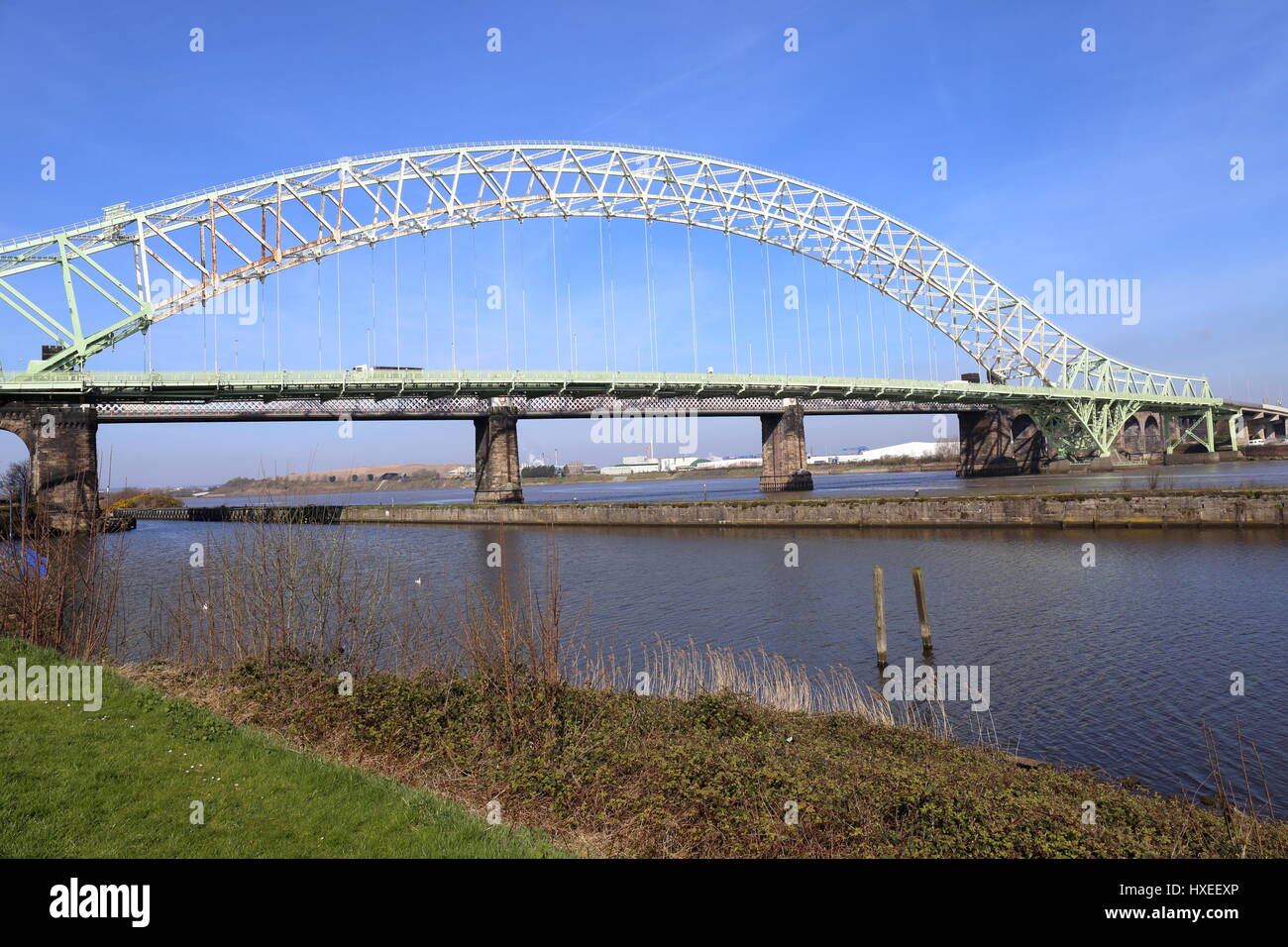 The Silver Jubilee Bridge at Runcorn crossing the Manchester Ship Canal and the River Mersey. Rail bridge of stone construction with pillars is behind Stock Photo