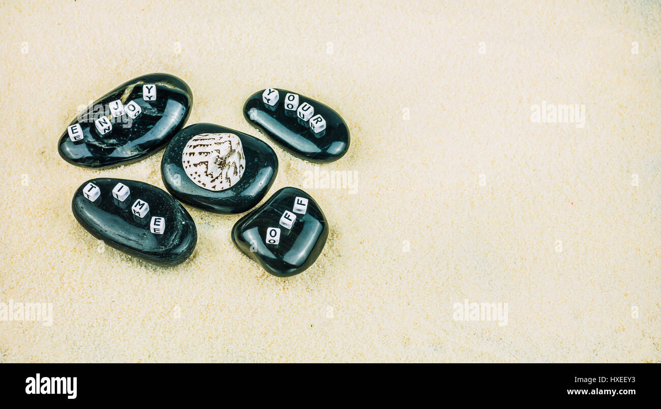 Enjoy your time off cube letters on black stones on sandy background Stock Photo