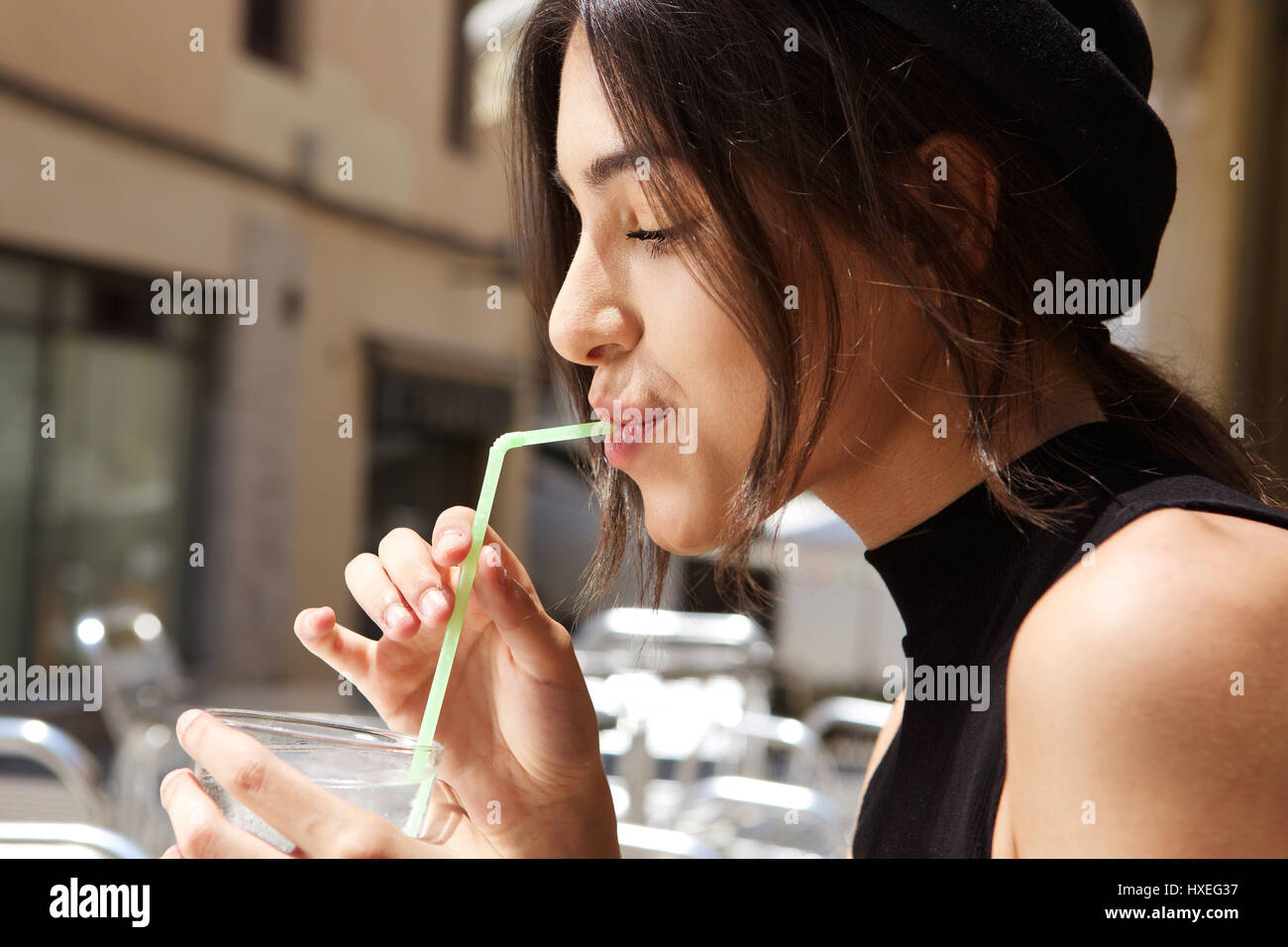 Close up side portrait of a young woman drinking with straw at outdoor cafe Stock Photo
