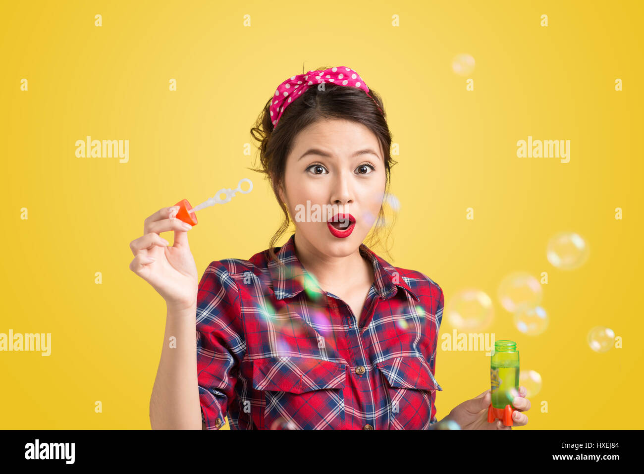 Pinup model blowing soap bubbles over yellow background. Stock Photo