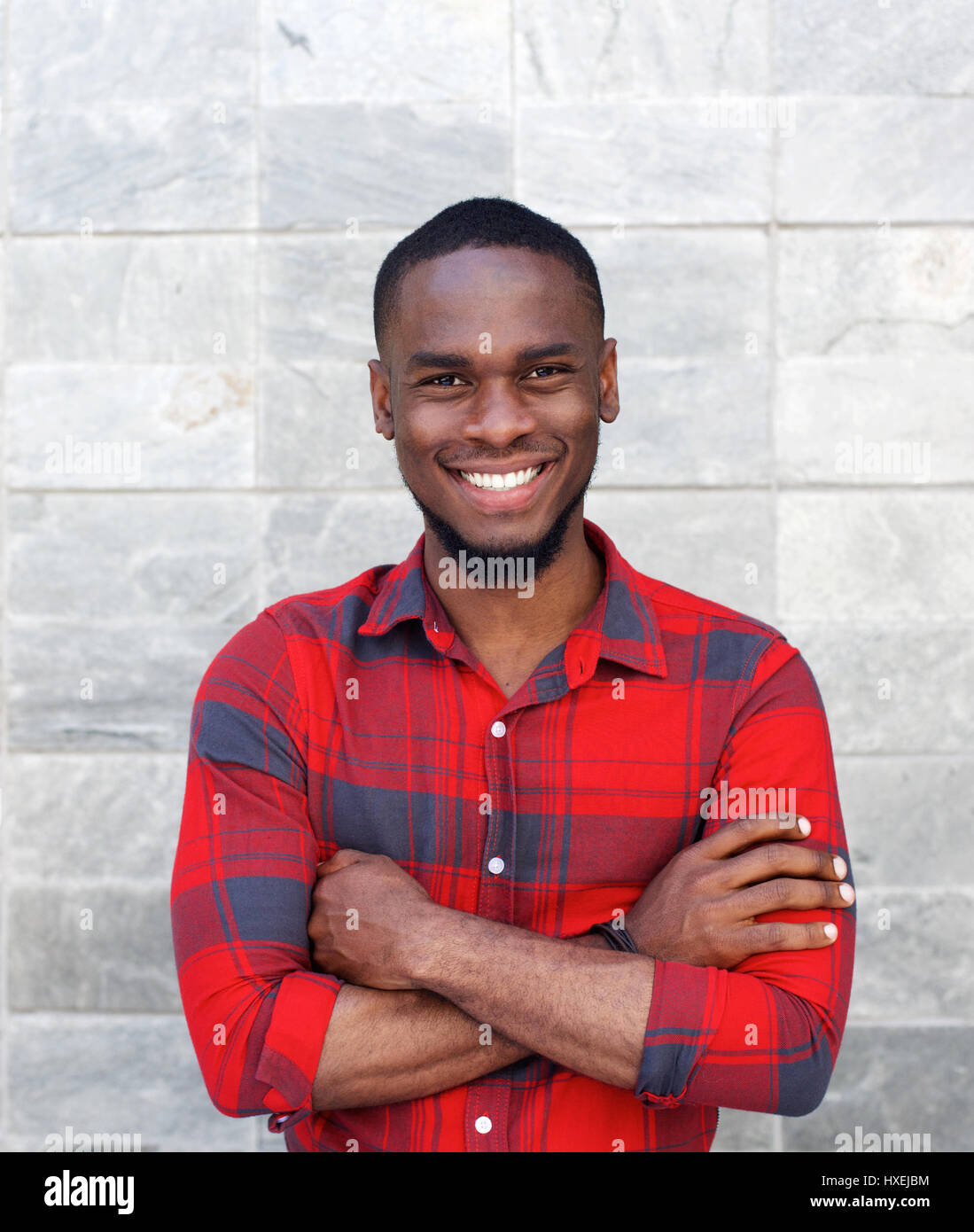 Portrait of a happy young black guy smiling with arms crossed while ...