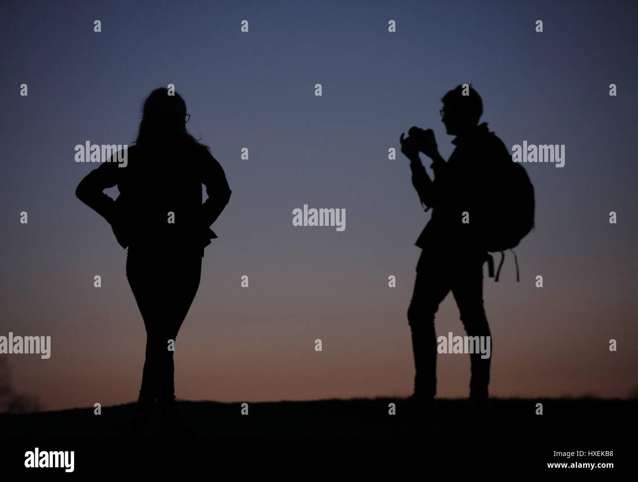 The silhouettes of a man photographing a woman at dusk on Parliament Hill, Hampstead Heath, north London. Stock Photo