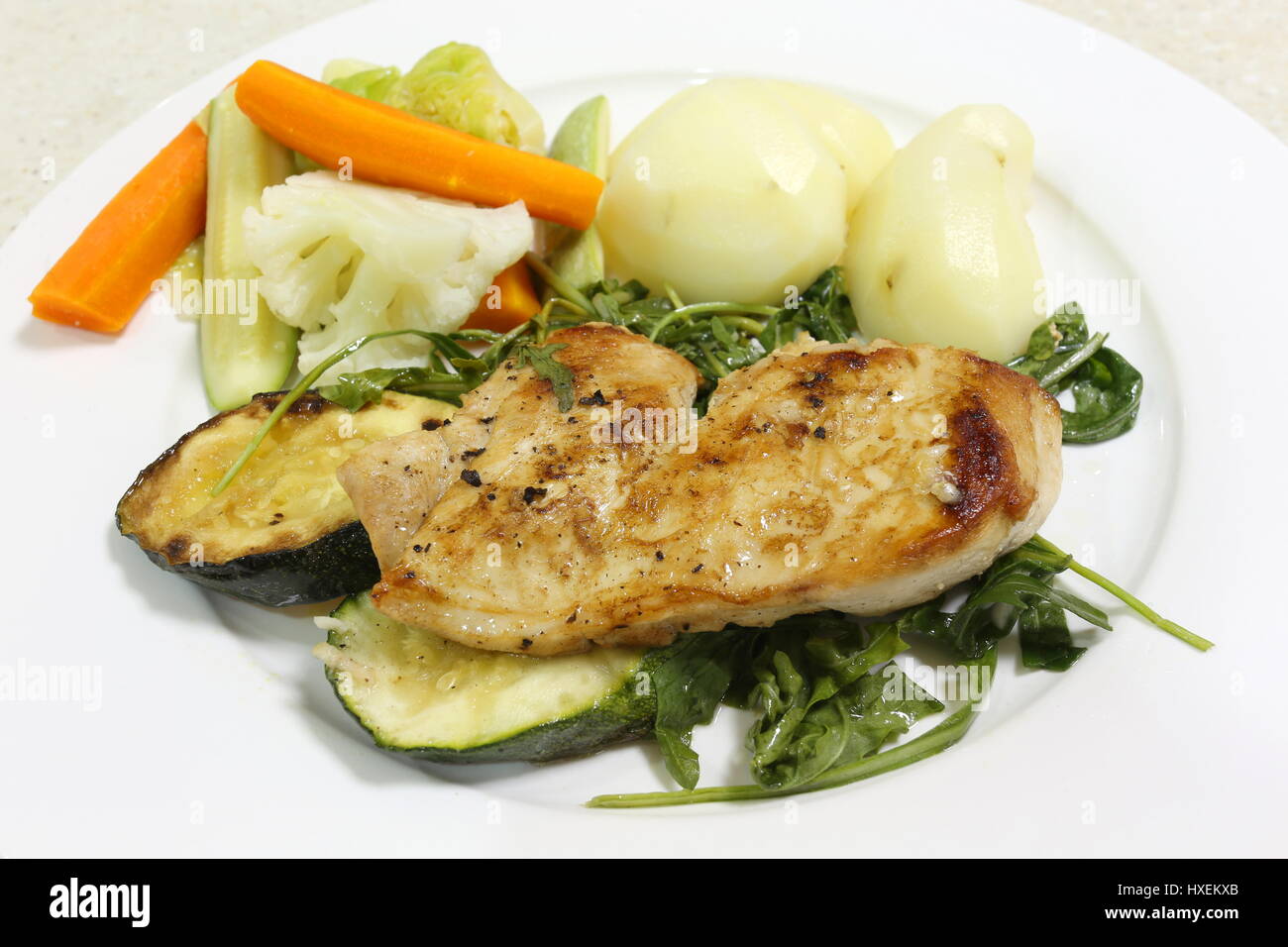 Grilled chicken on a bed of boiled rocket or aragula, served with potatoes and a mixture of steamed vegetables Stock Photo