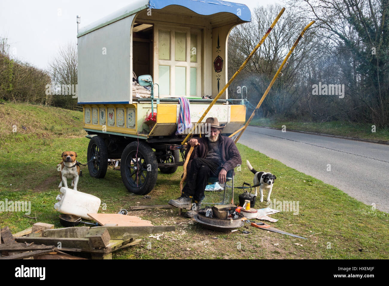 An elderly traveller and his horse and two dogs sit outside his traditional wagon by a brazier Stock Photo