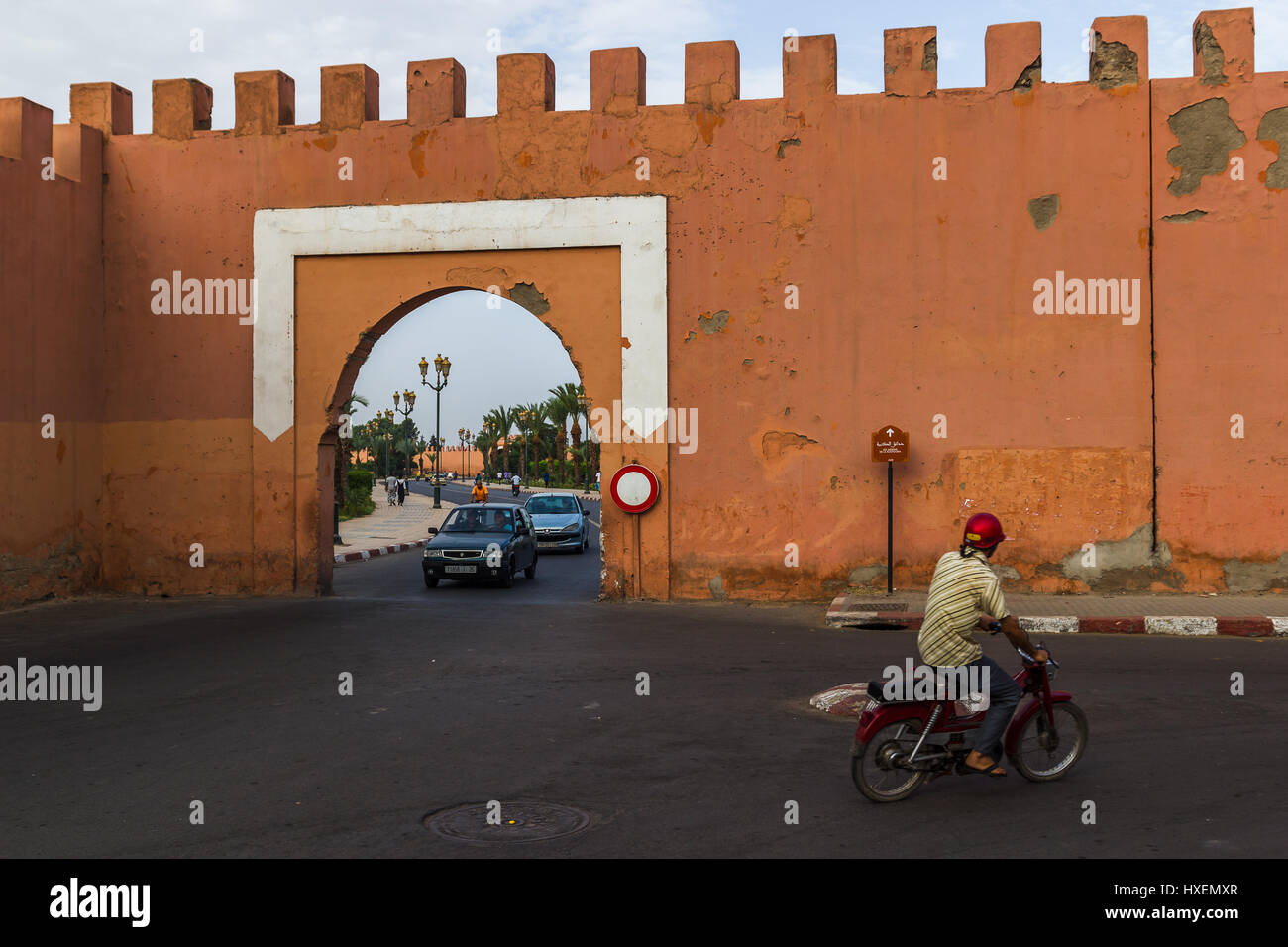 Traffic flows through a gateway in the walls which surrounds most of the 'red city' known as Marrakesh.  The name 'red city' comes from the pinky/oran Stock Photo