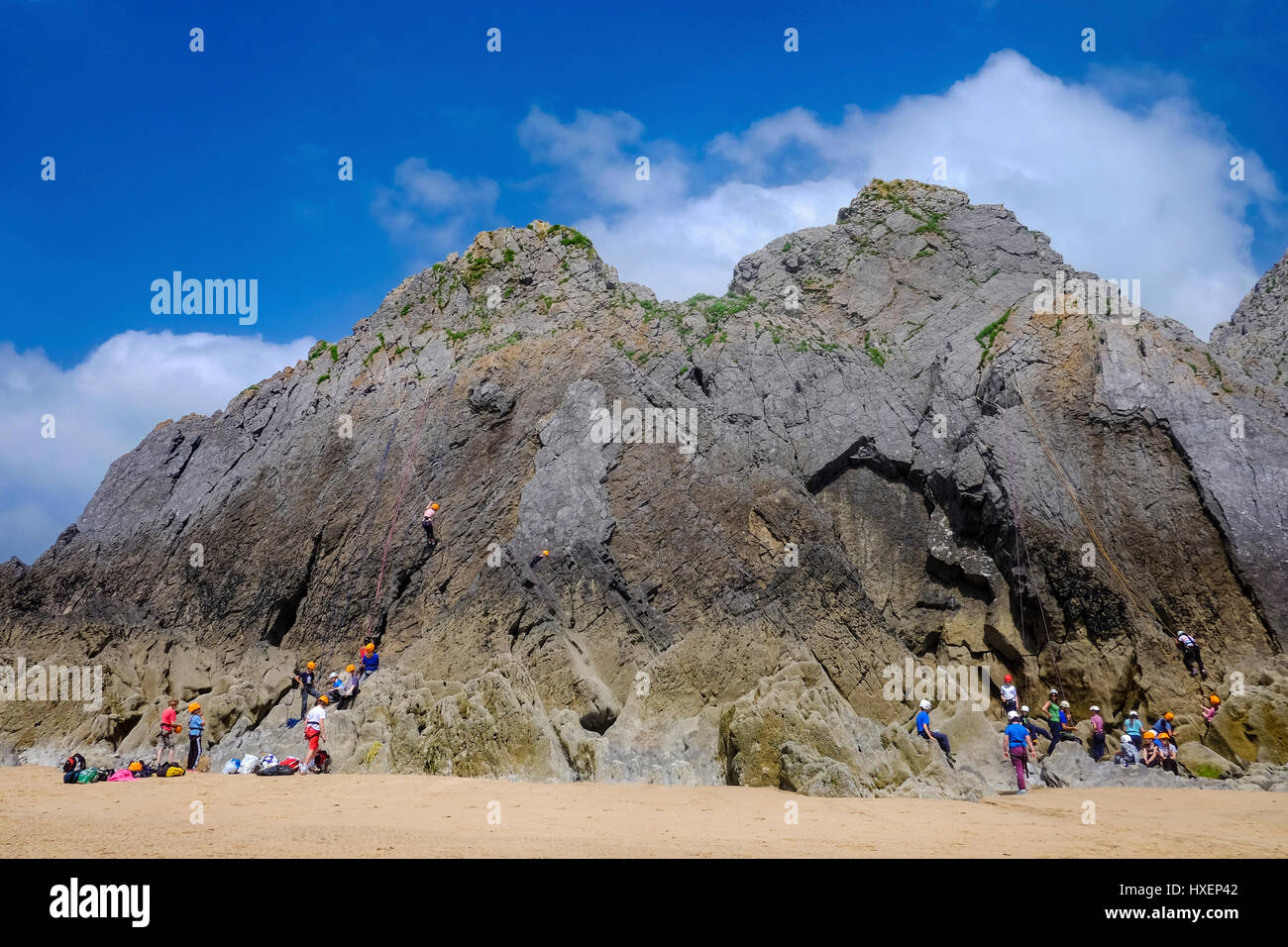 Group of school children rock climbing at Three Cliffs Bay, Gower Peninsula, South Wales, UK Stock Photo