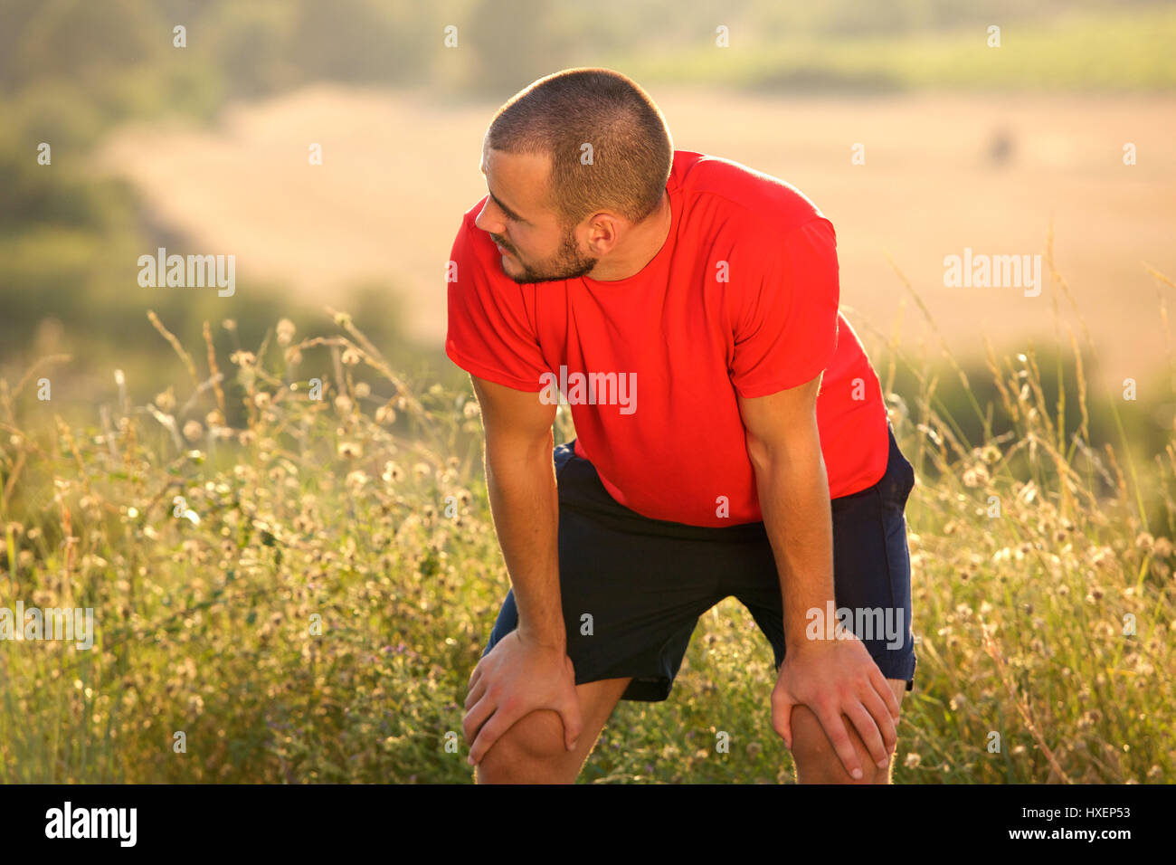 Tired young man bending down with hands on knees after workout exercise ...