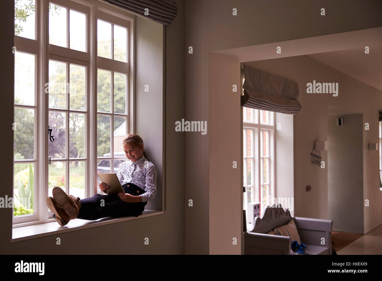 Girl Sits By Window At Home Using Digital Tablet Stock Photo