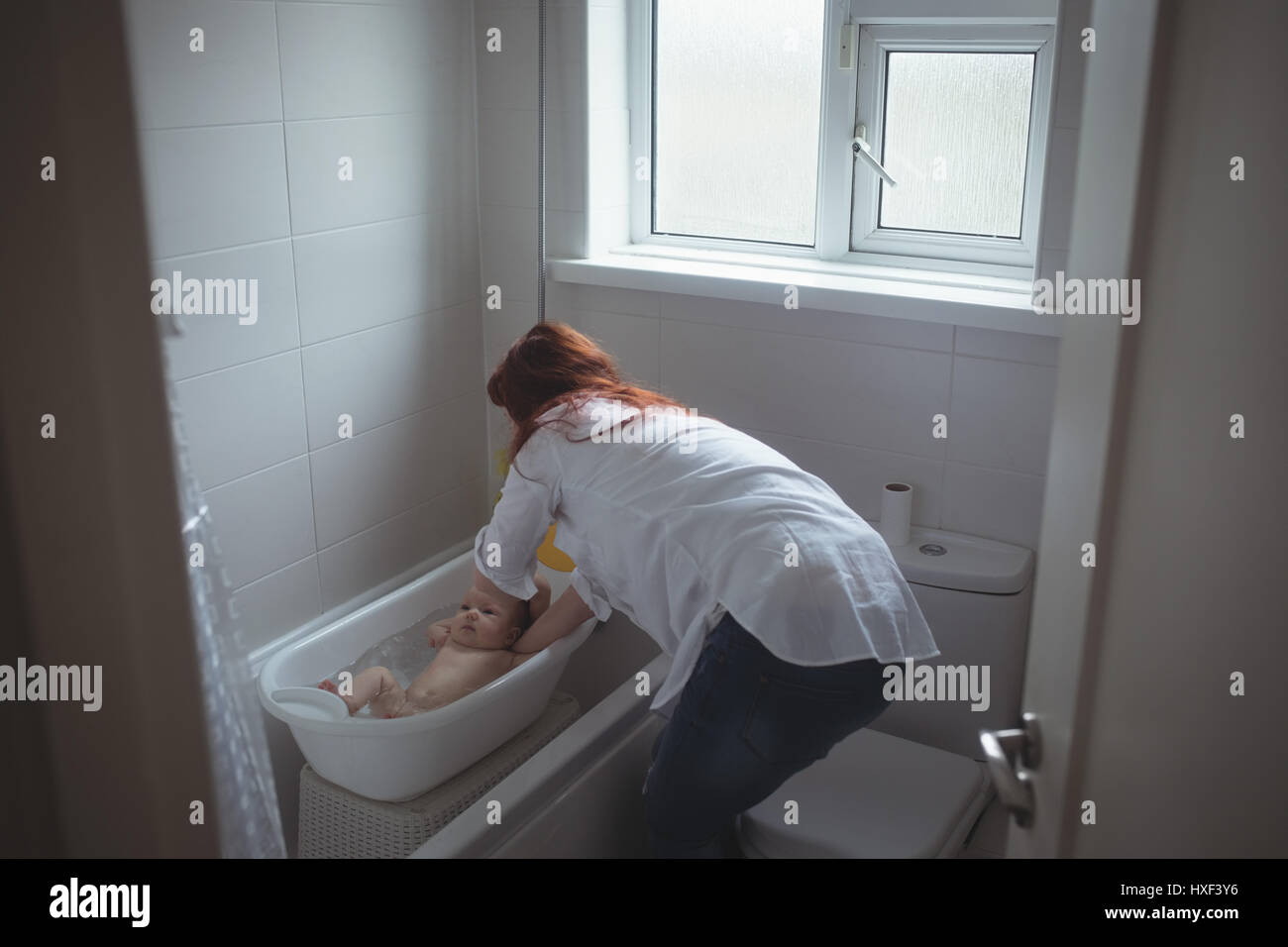 Mother washing baby in bathtub seen from open door Stock Photo Alamy