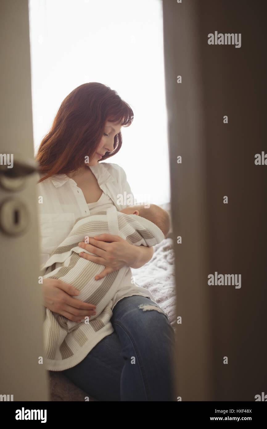 Mother breastfeeding baby while sitting on bed at home Stock Photo Alamy