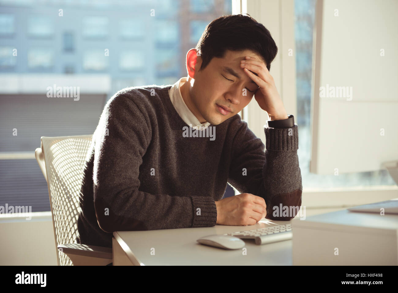 Depressed male executive sitting at desk in office Stock Photo