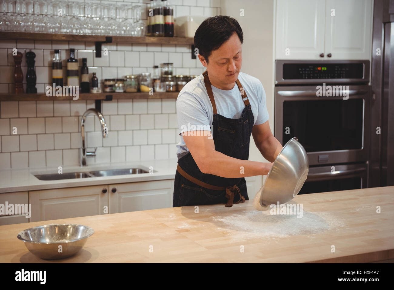 Male chef emptying flour on counter top at restaurant Stock Photo