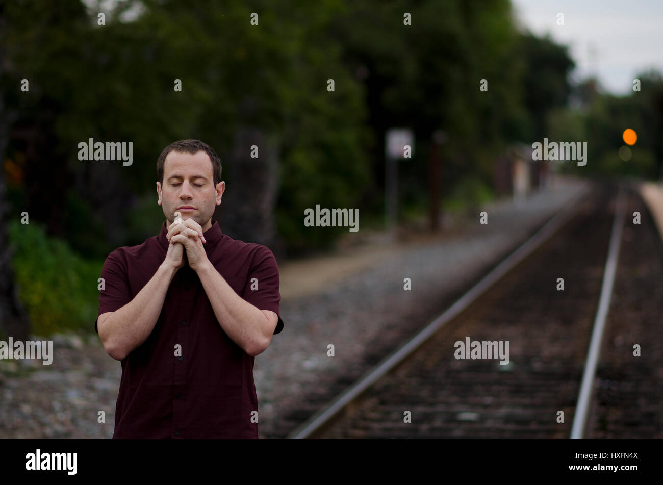 Man praying alone by train tracks with hands clasped together. Stock Photo