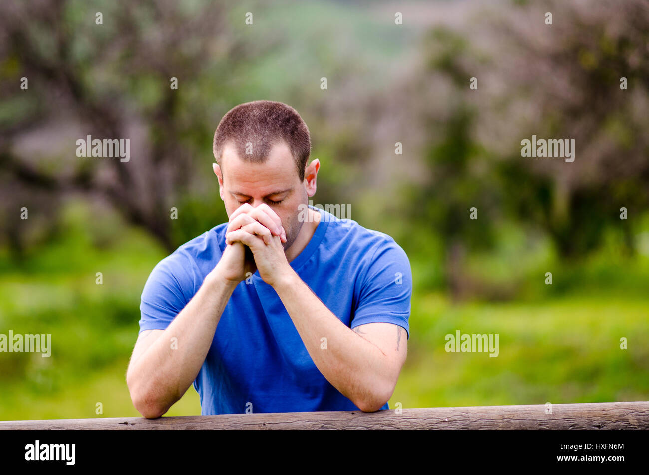 Man praying with his head down and hands together, alone in nature embracing God`s creation. Stock Photo