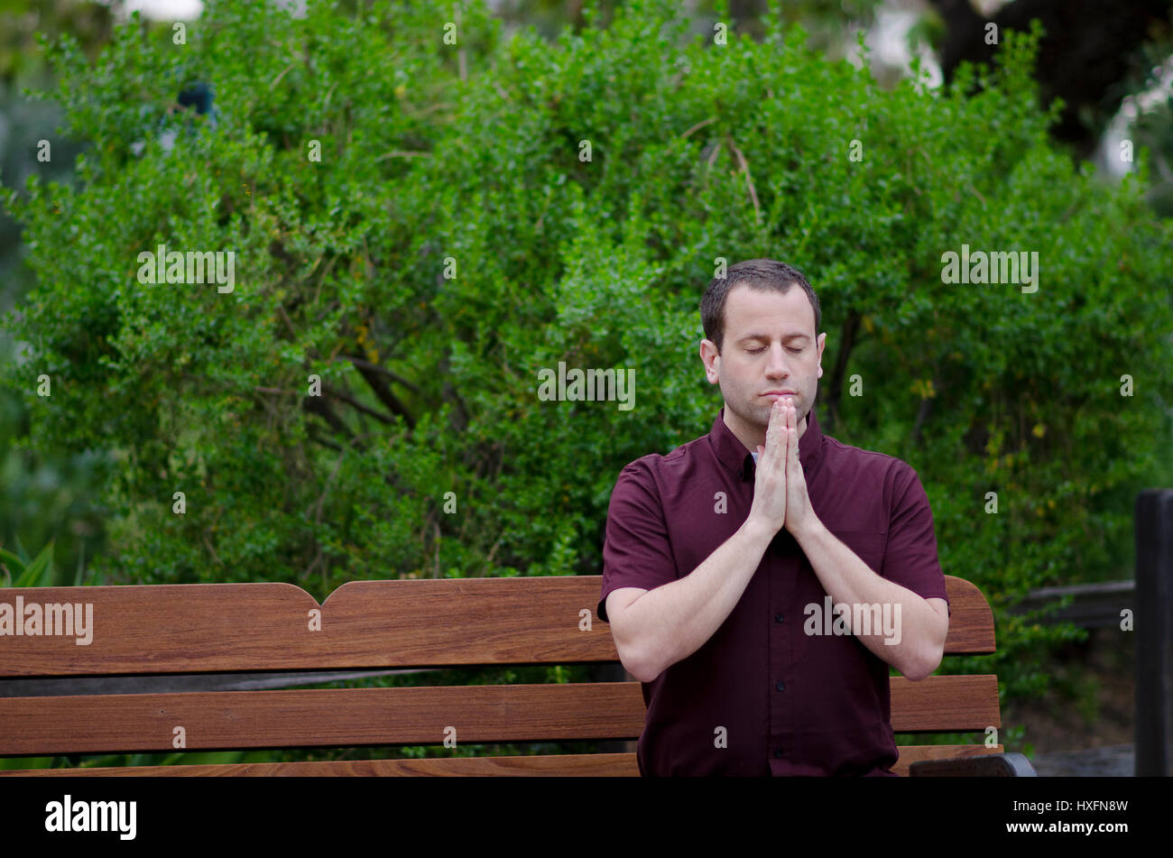 Man praying with hands together on a bench outside. Stock Photo