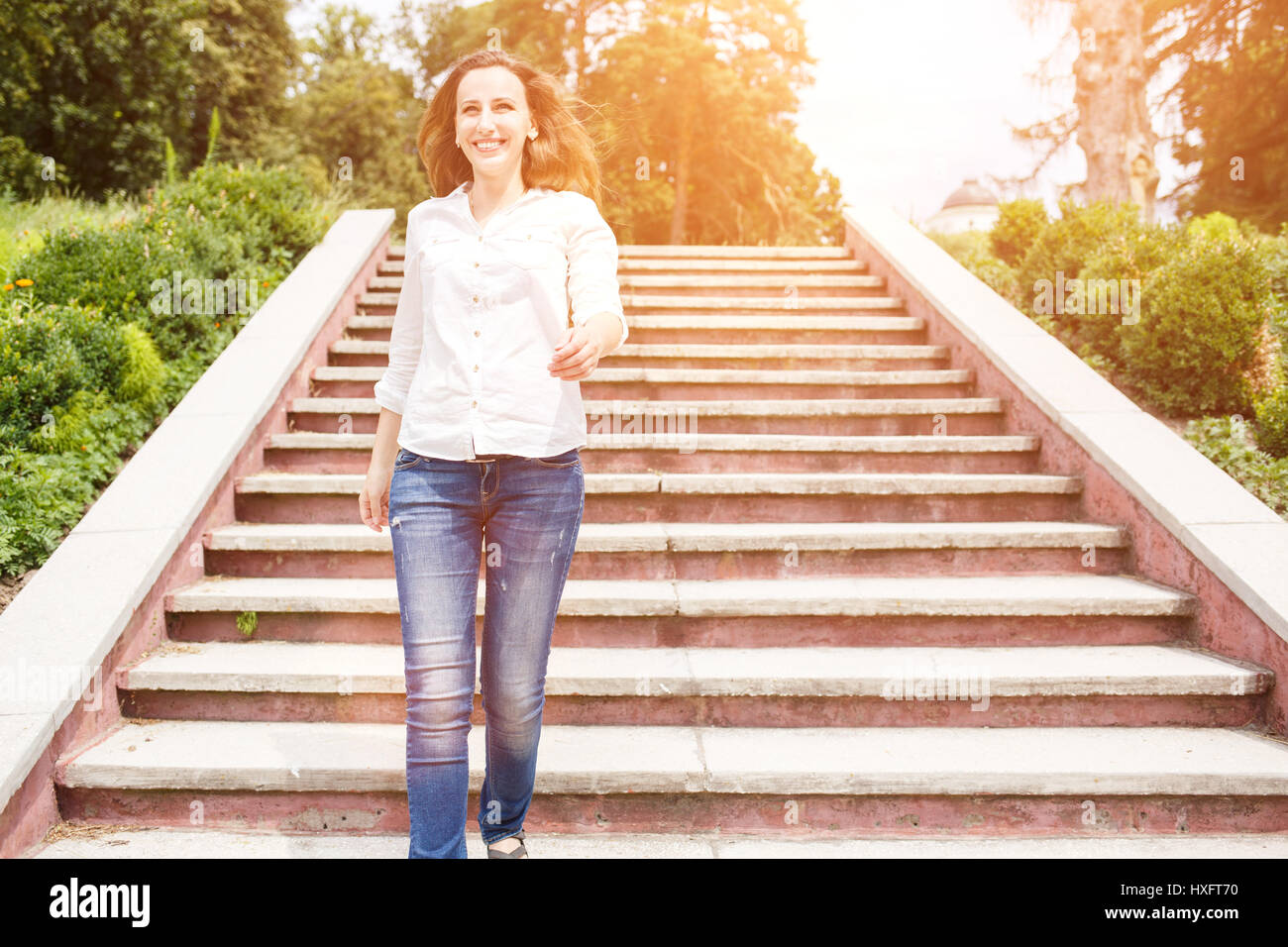 Happy young woman in white shirt going down the stairs in park Stock Photo