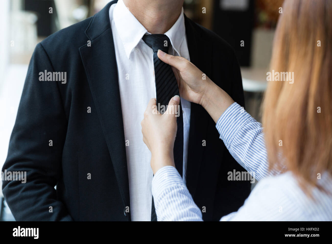 Woman's hands adjusting black tie of man in suit. Wife helping his husband to get dressed. Clothes detail. Stock Photo