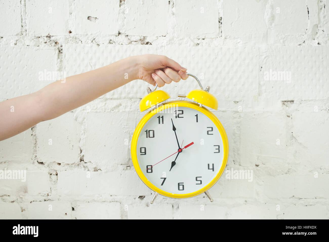 Girl's hand holding yellow alarm clock isolated on white brick backgroung, closeup Stock Photo