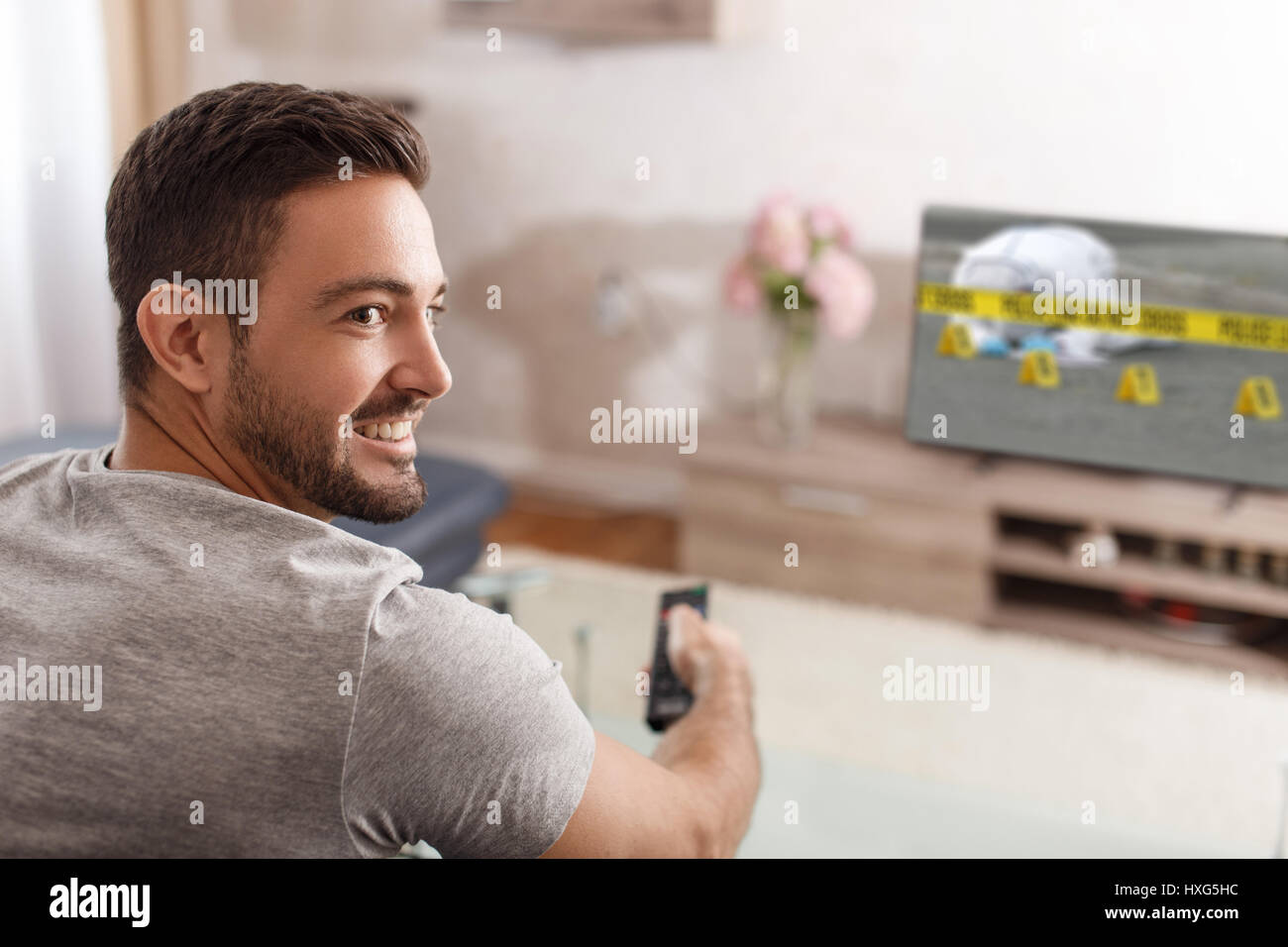 Excited man switch TV to crime serie by remote control Stock Photo