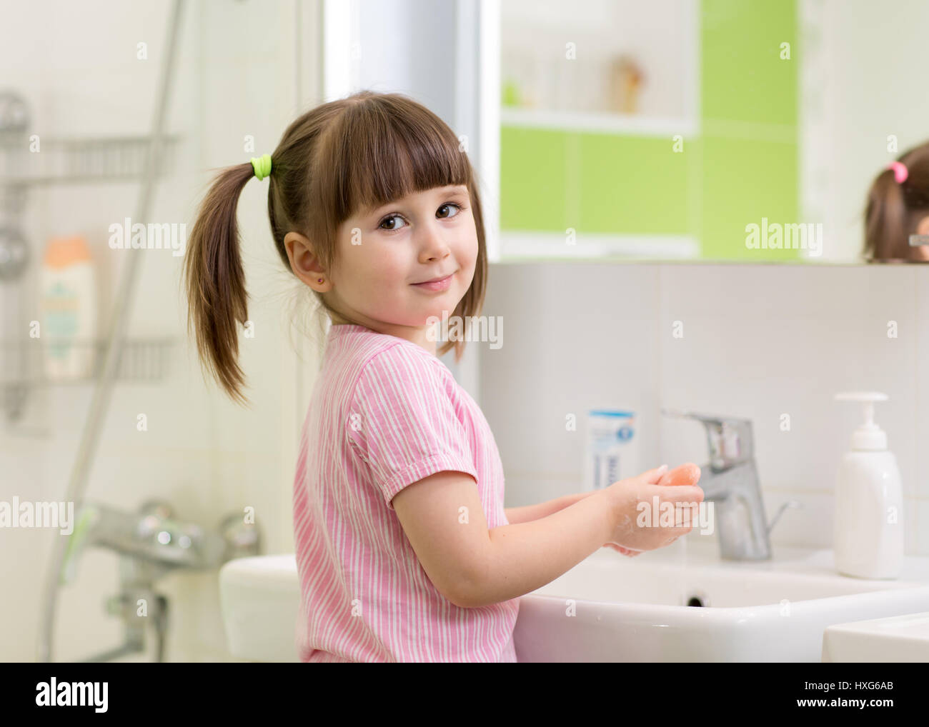 Cute kid girl with ponytail in pink bathrobe washing her hands. Stock Photo