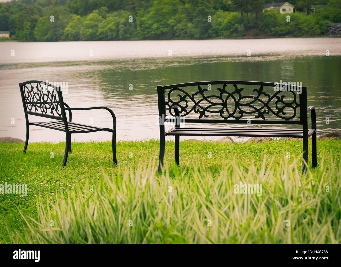 Decorative metal park benchs overlooking still water. Stock Photo