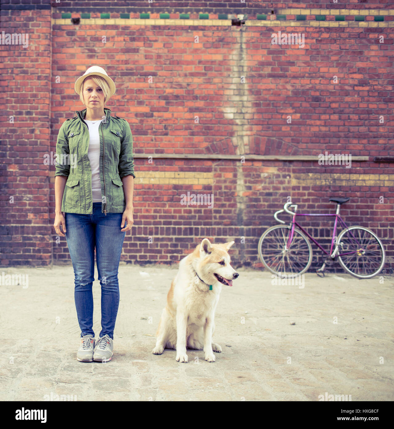 Hipster young beautiful girl with vintage road bike in city relaxing with akita inu dog, urban scene. Woman commuter cycling on fixed gear bike in tow Stock Photo