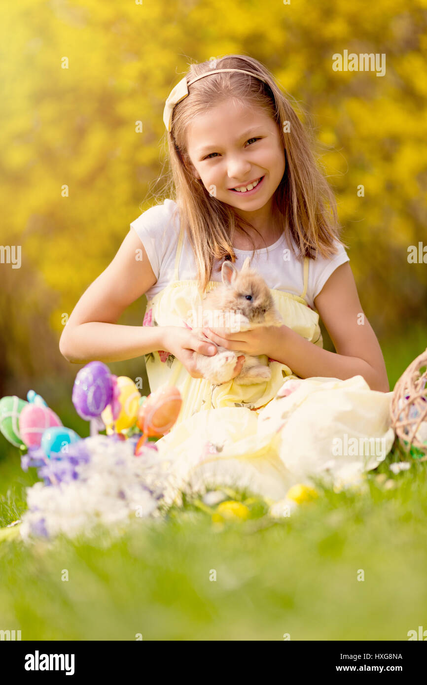 Beautiful smiling little girl holding cute bunny and sitting on the grass in spring holidays. Stock Photo