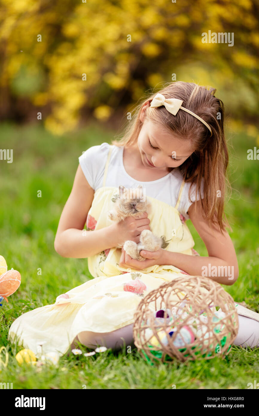 Beautiful smiling little girl holding cute bunny and sitting on the grass in spring holidays. Stock Photo