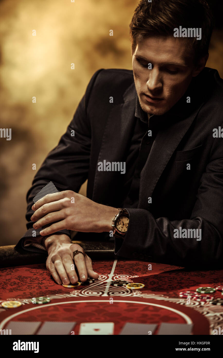 Serious man in suit holding playing cards and poker chips in casino Stock Photo