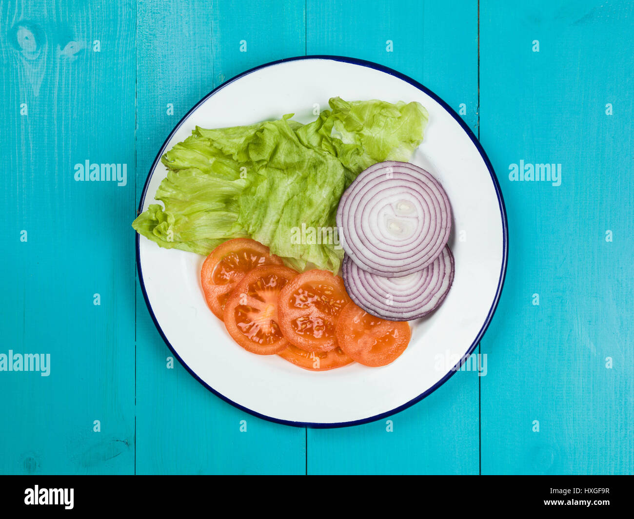 Fresh Garden Salad Tomato Onion and Lettuce Against a Blue Background Stock Photo
