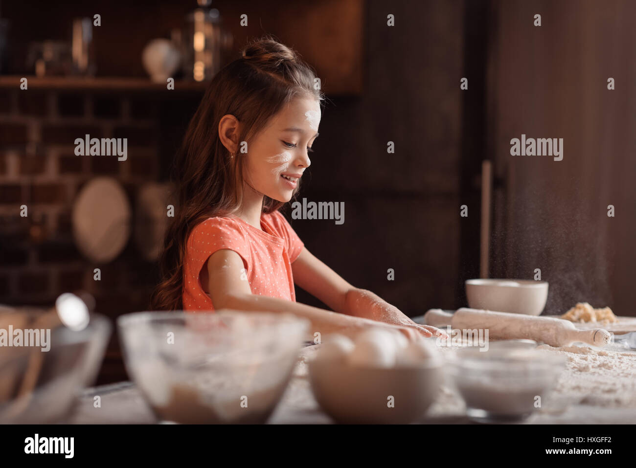 'Side view of smiling little girl with flour on face kneading dough ...