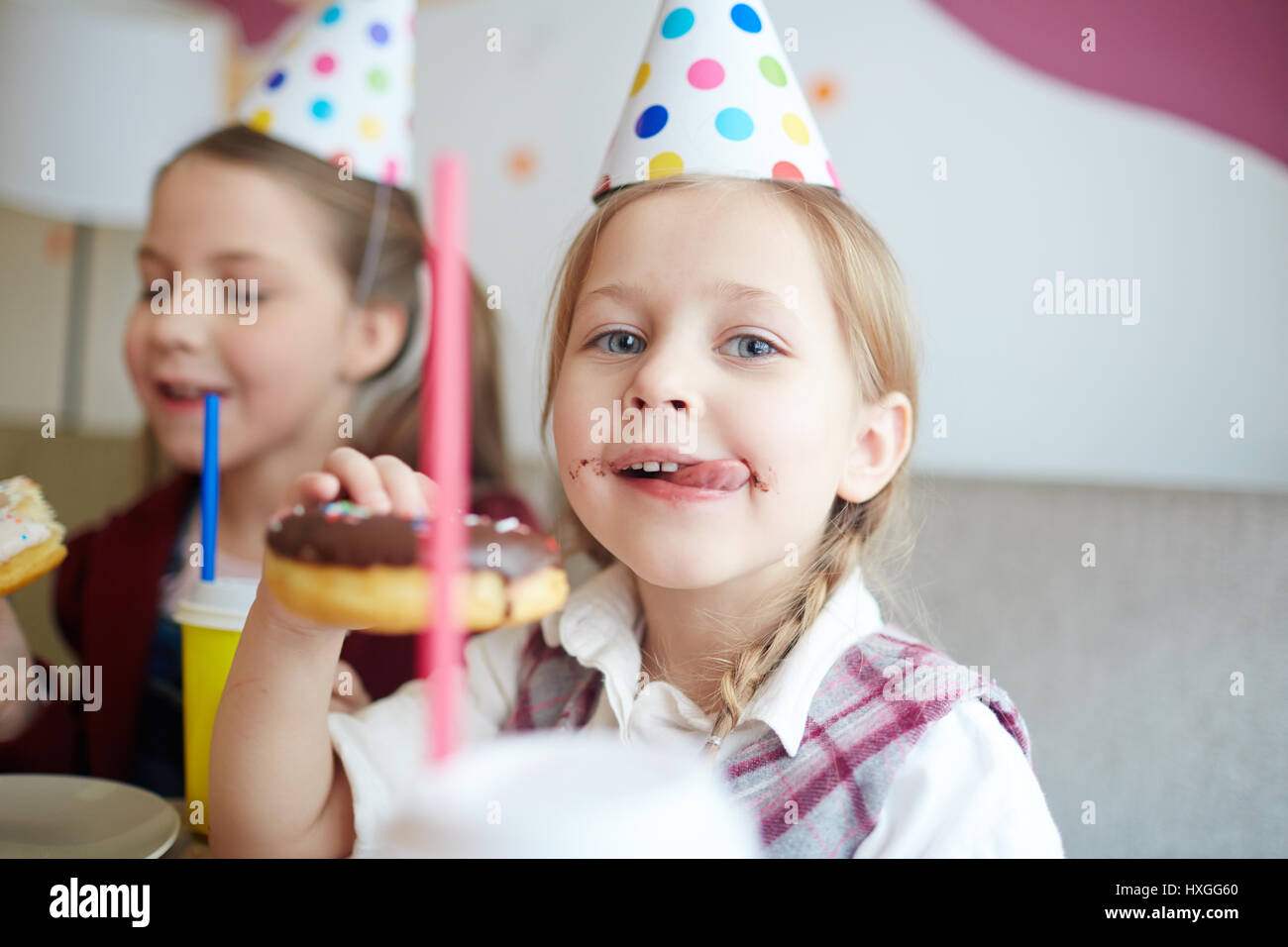 Cute girl licking her lips while eating yummy donut with chocolate glaze Stock Photo