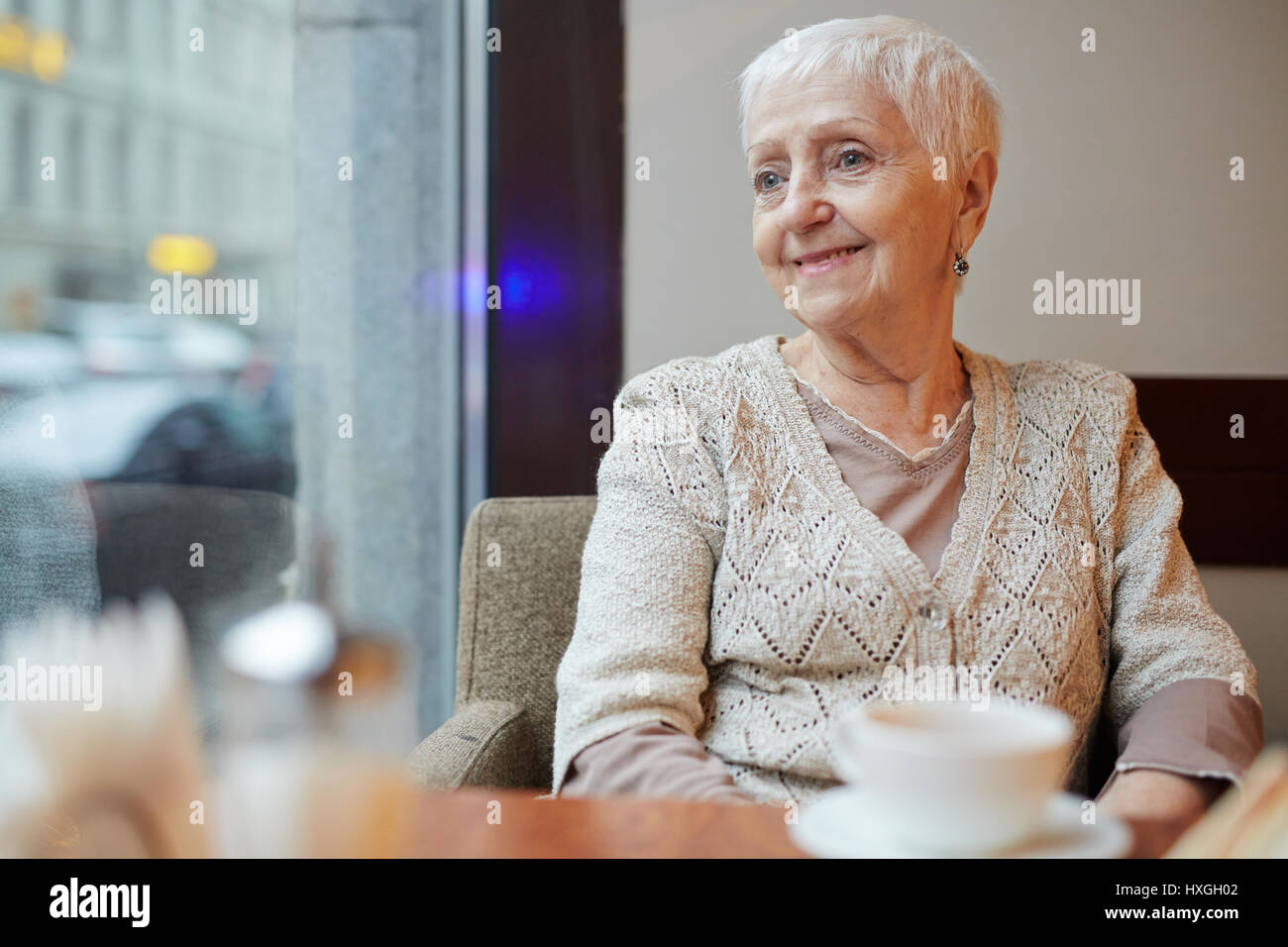 Smiling grandmother sitting in arm-chair and looking through window ...