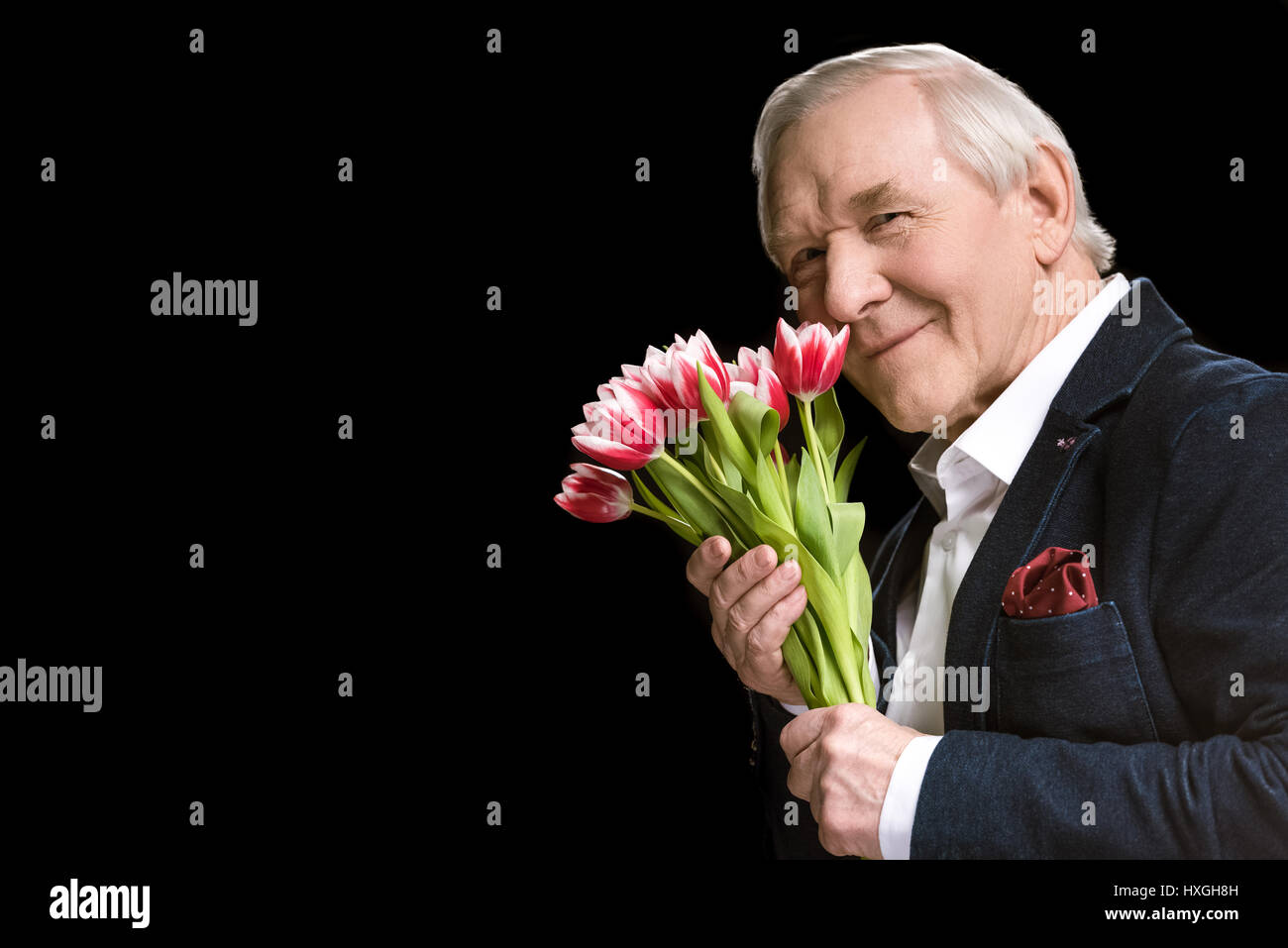 Senior man in suit holding beautiful tulips and smiling at camera, spring holiday concept Stock Photo