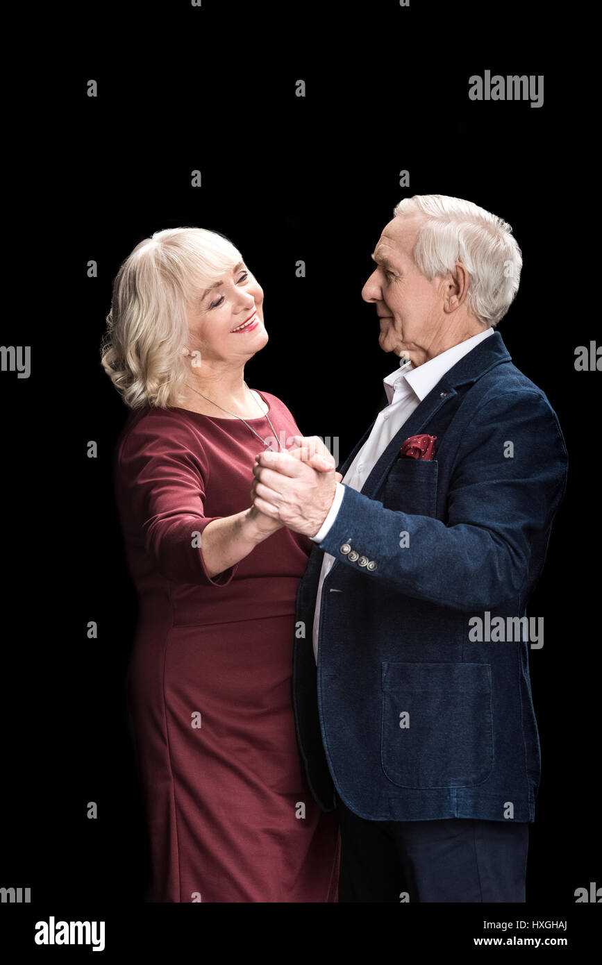 Side view of beautiful happy senior couple dancing on black Stock Photo