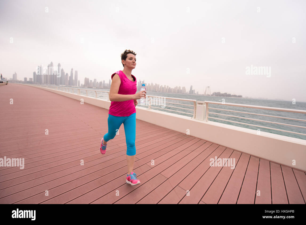 very active young beautiful woman busy running on the promenade along ...
