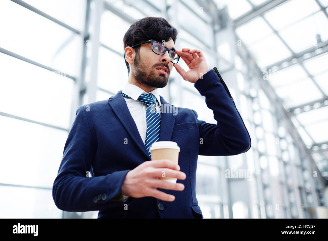 Posh young man in suit and eyeglasses holding drink Stock Photo
