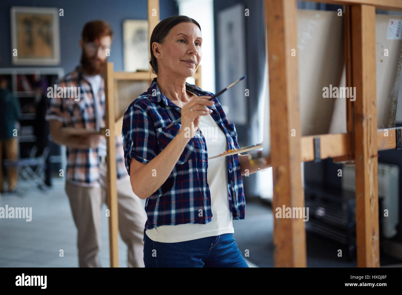 Elderly woman looking at painting on easel while working in studio of art Stock Photo
