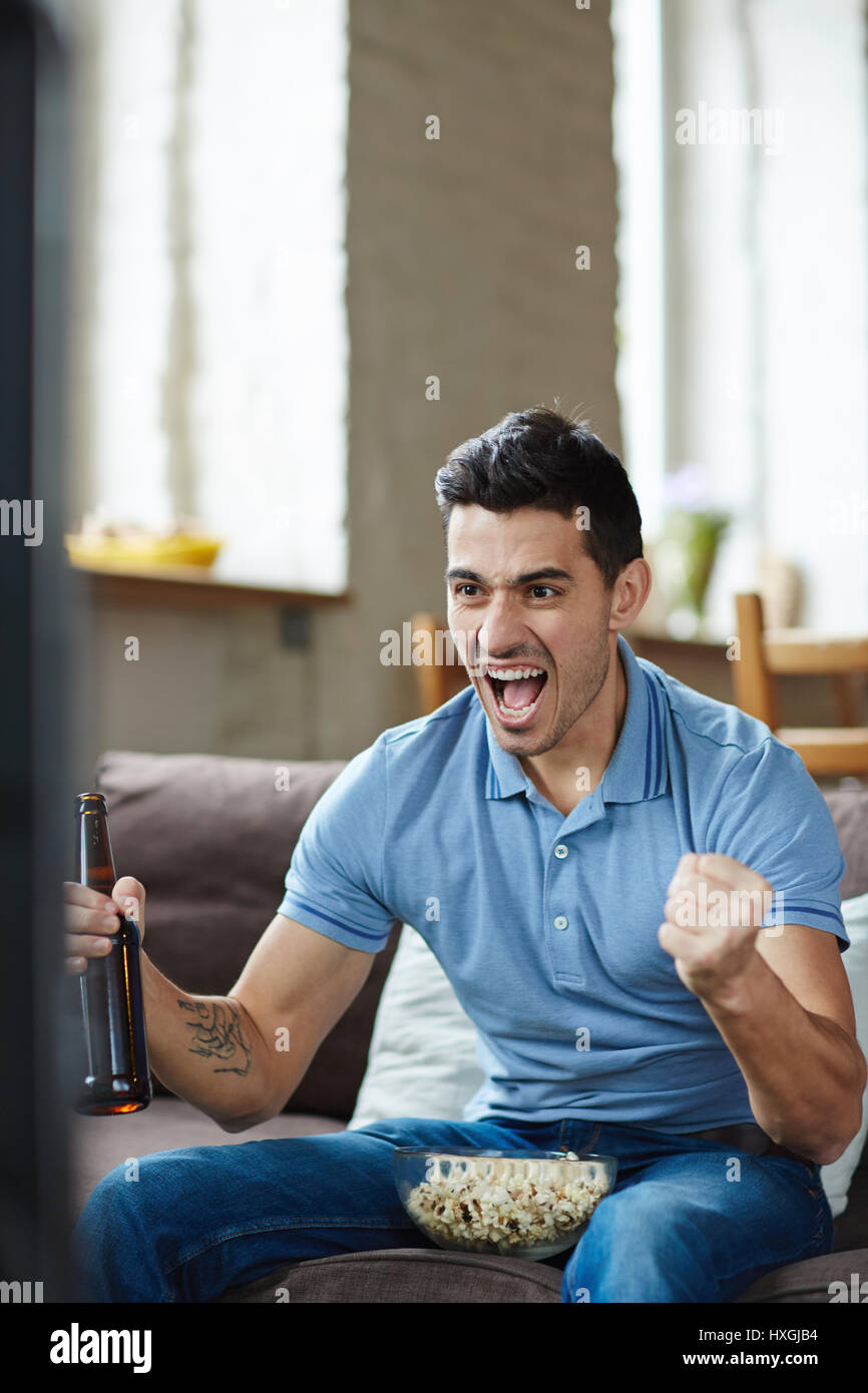 Portrait of emotional sports fan watching match on tv, cheering joyfully and screaming with