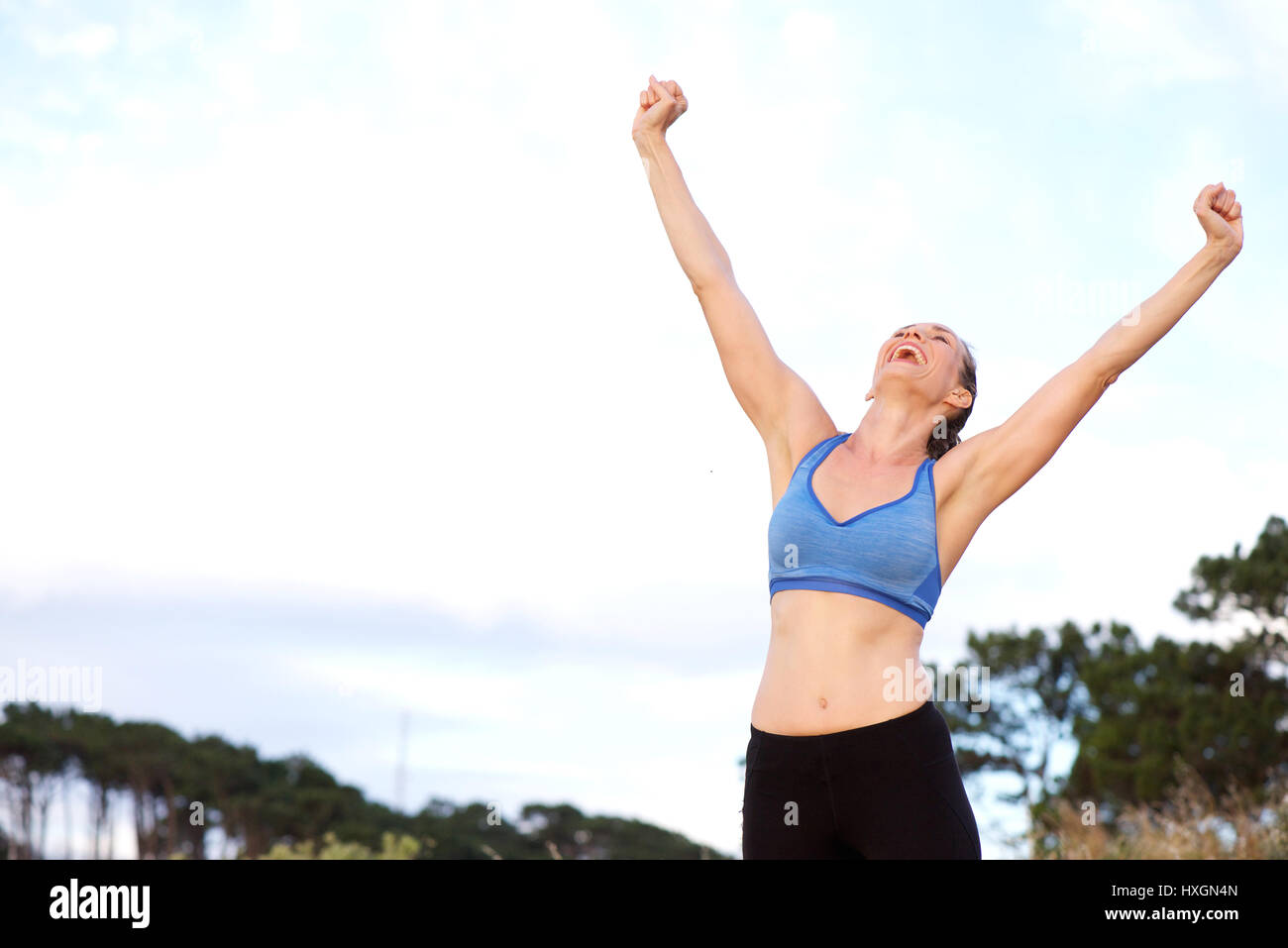 Portrait of woman cheering with arms raised outdoors Stock Photo - Alamy