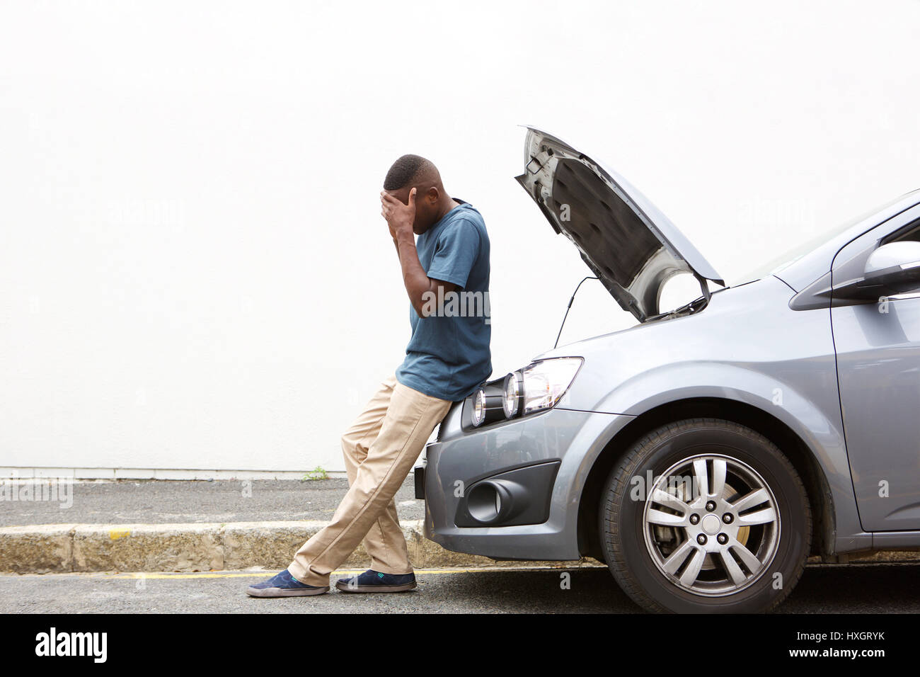 Full length portrait of upset young african man standing in front of a broken down car parked on the side of a road Stock Photo