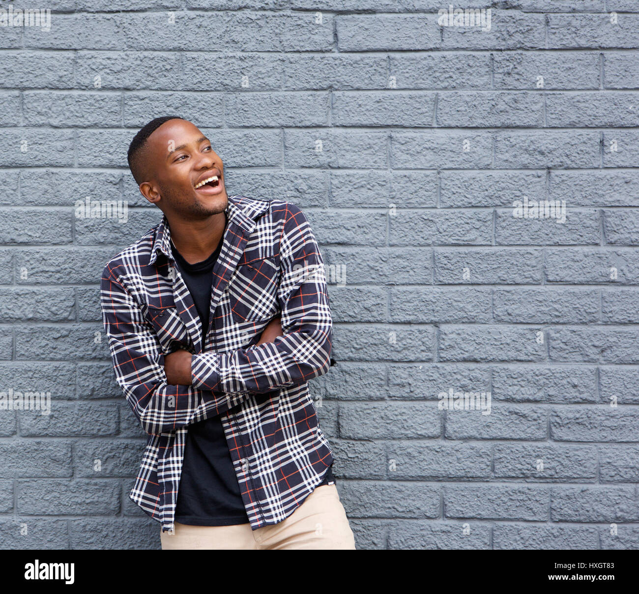 Portrait of a happy young black man smiling with arms crossed against ...