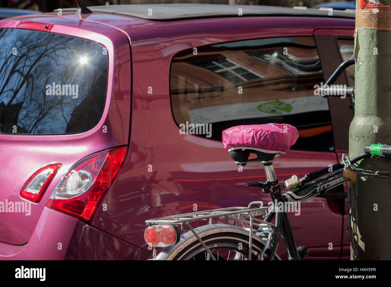 A bicycle with a pink saddle stands in front of a car with the same pink paint. Stock Photo