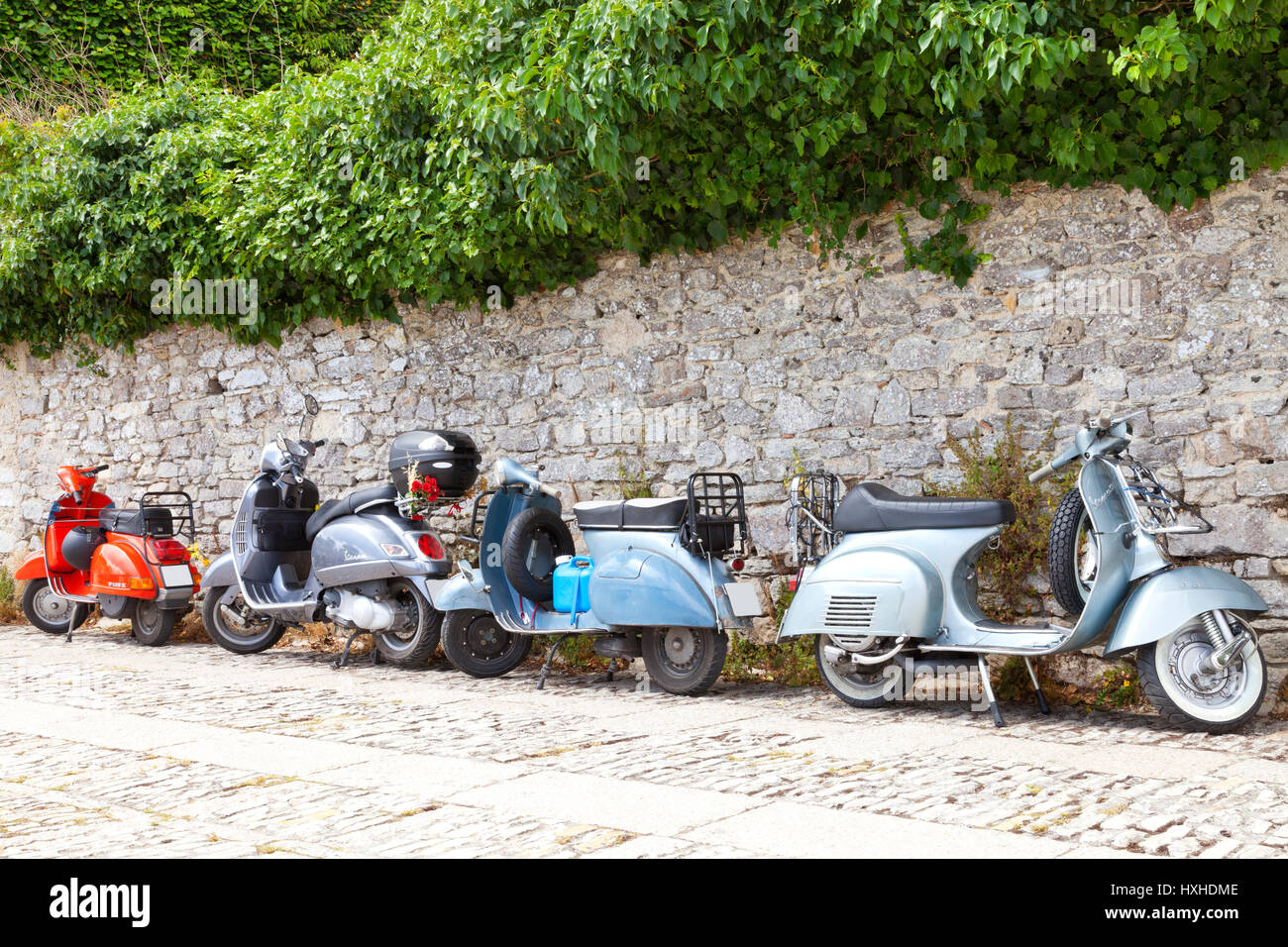Erice, Sicily, Italy - June 13 2016: Red and blue retro Italian scooters Vespa parked on a road by a stone wall . Stock Photo