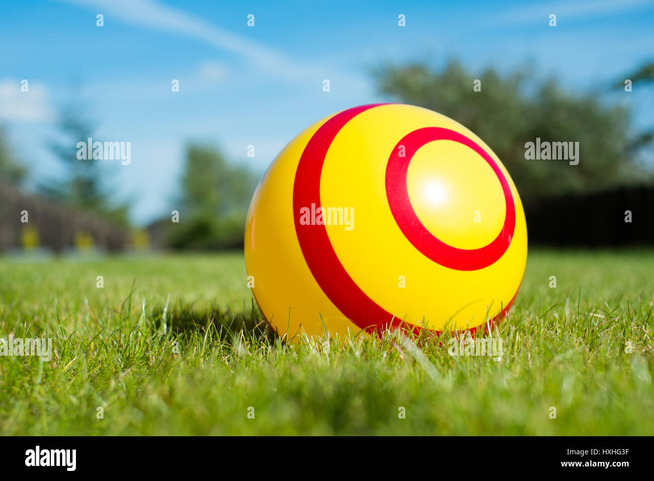 a red and yellow striped child's ball sits on a luscious green lawn ...