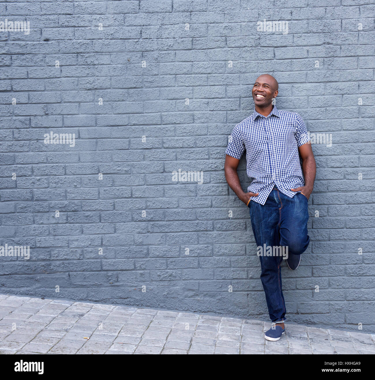 Full length portrait of smiling african guy leaning against gray wall ...