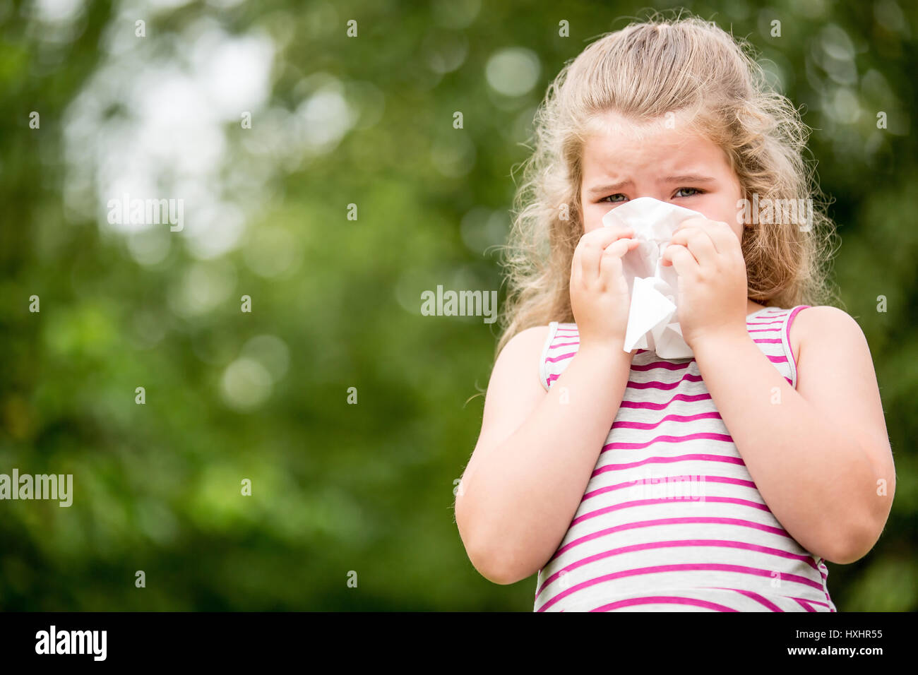 Ill child with a cold or flu sneezes and cleans nose with tissue Stock Photo