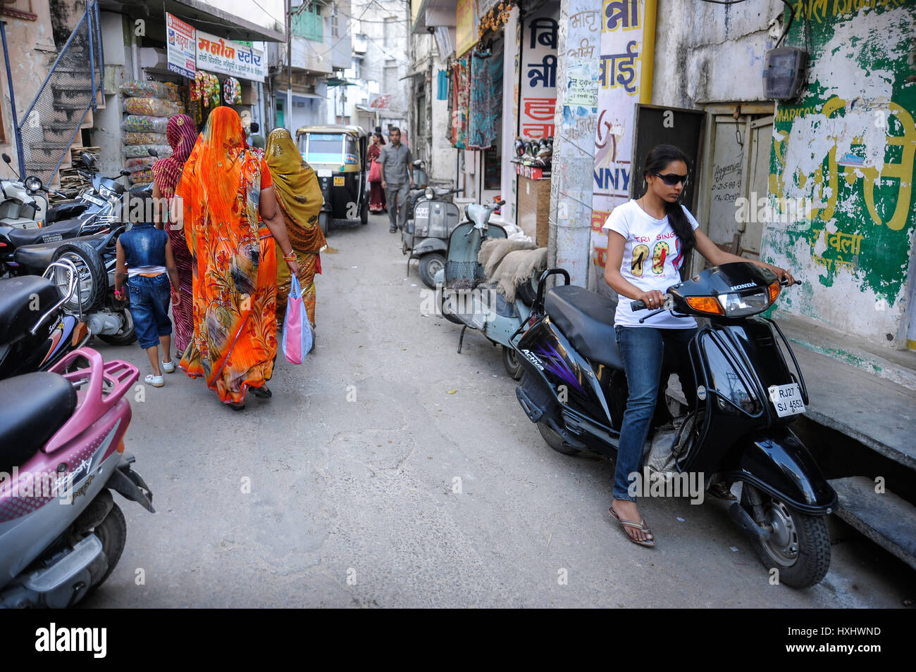 Street scene in Udaipur with women in traditional dress and young girl in modern dress on a moped Stock Photo